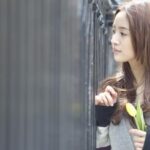 Young woman holding yellow tulip near fence