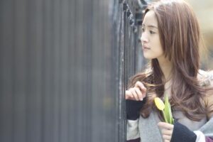 Young woman holding yellow tulip near fence
