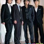 Four men in black suits posing together