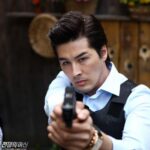Man in vest pointing pistol at camera
