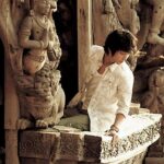 Seated person in white shirt amid intricate carvings