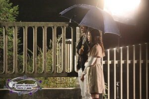 Two people under umbrella on bridge at night