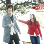 Two smiling people walking outdoors under a tree