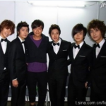 Six men in tuxedos posing and smiling