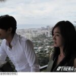 Two people on balcony overlooking coastal cityscape