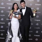 Two people holding trophies on red carpet