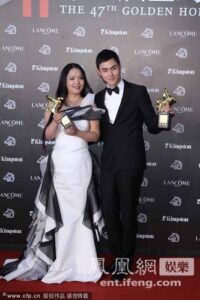 Two people holding trophies on red carpet