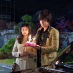 Young couple holding birthday cake beside car