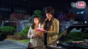 Young couple holding birthday cake beside car