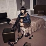 Woman on bed removing boots, shoes scattered