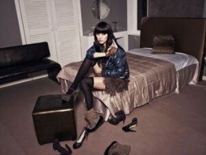 Woman on bed removing boots, shoes scattered