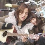 Two women outdoors, one playing guitar, one resting