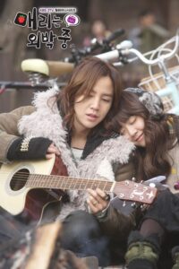 Two women outdoors, one playing guitar, one resting