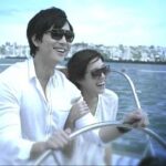 Smiling pair wearing sunglasses steering boat at sea