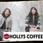 Two women biking beneath trees, Hollys Coffee sign