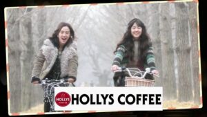 Two women biking beneath trees, Hollys Coffee sign