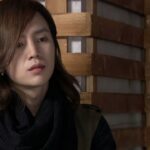 Long-haired person leaning against wooden slats