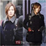 Long-haired person in black peacoat carrying guitar