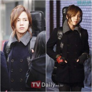 Long-haired person in black peacoat carrying guitar