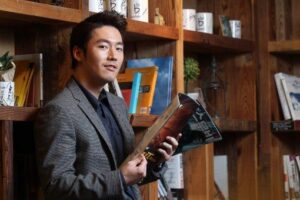 Man holding magazine by wooden bookshelf