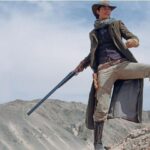 Cowboy standing on rocky hill holding shotgun