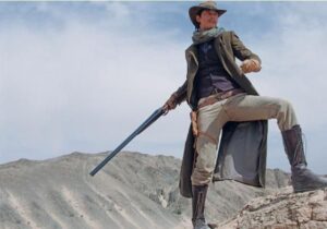 Cowboy standing on rocky hill holding shotgun