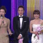 Three presenters on stage holding flowers and microphone