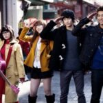 Four young people saluting on street, pink guitar