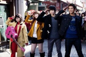 Four young people saluting on street, pink guitar