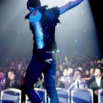 Performer with raised arm on spotlighted stage