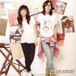 Two young people posing by poster-covered wall