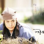Young man in traditional Korean attire crouching outdoors