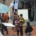 Actors on outdoor film set surrounded by crew