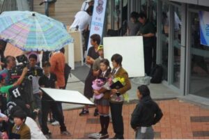 Actors on outdoor film set surrounded by crew