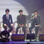 Three men in suits seated on stage