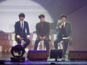 Three men in suits seated on stage