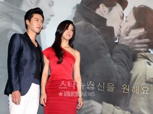 Actors posing in front of romantic movie poster