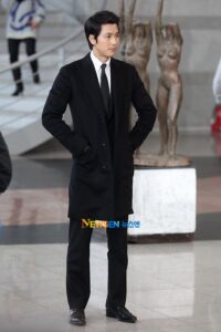 Man in black suit standing near sculpture