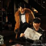 Two men smiling, one reading a newspaper