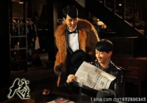 Two men smiling, one reading a newspaper