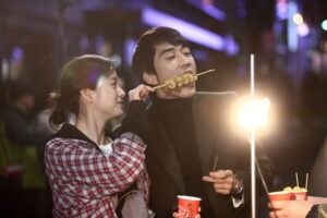 Couple sharing skewered street food at night