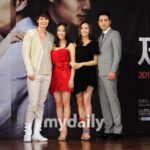Four people posing in front of promotional poster