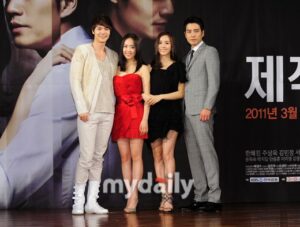 Four people posing in front of promotional poster