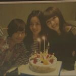 Three women smiling behind a birthday cake