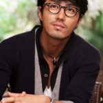 Seated man with glasses, necklace, and cardigan
