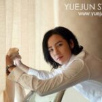 Person in white shirt adjusting curtain by window