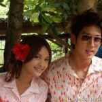 Smiling couple outdoors, woman with red flower