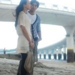 Two people standing on beach near bridge