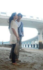 Two people standing on beach near bridge