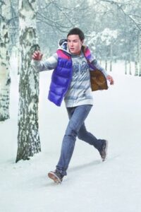 Young man running through snowy birch woods